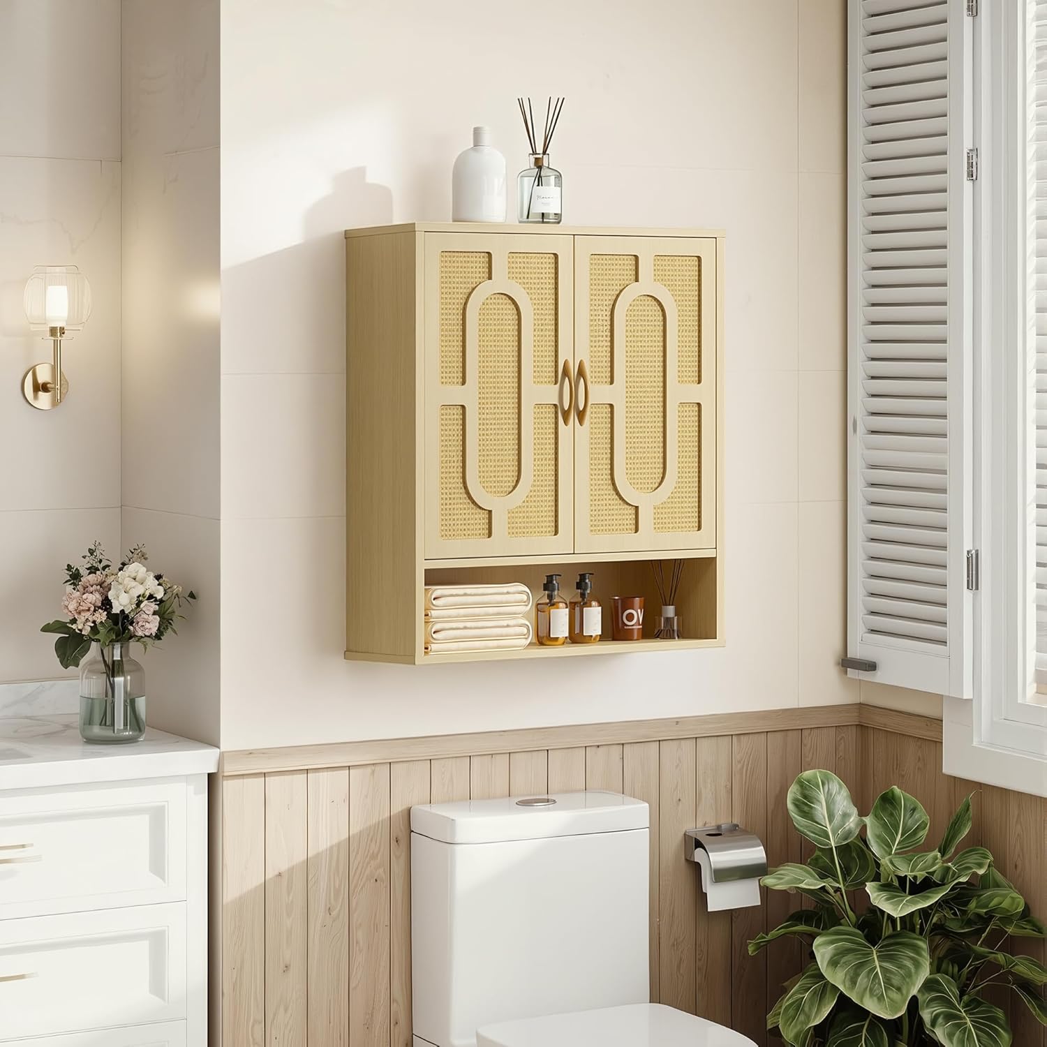 Wall-mounted bathroom storage cabinet in a light wood finish with woven panel doors, holding folded towels and toiletries above a toilet in a bright, modern bathroom.